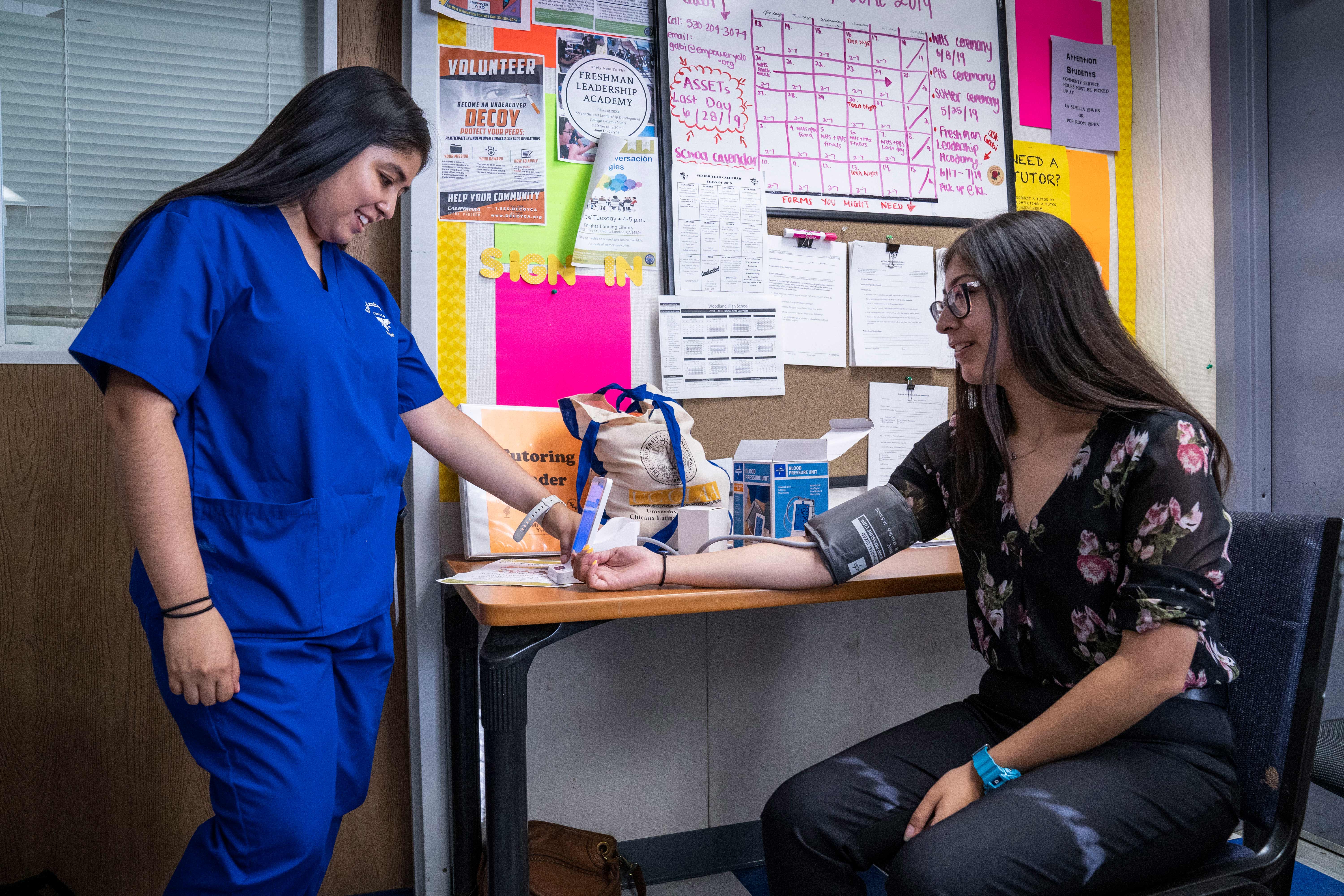 Clinical nutrition student Christina Roldan checks a blood pressure kit with global disease biology undergraduate Maria Hernandez at a Knights Landing clinic for medically underserved populations.