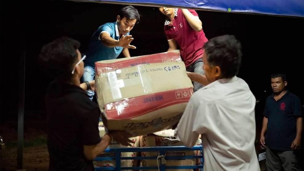 Lach Song, center left, guides a box of freshly packed vegetables onto a cart to wait for a late-night bus pickup that will deliver the farmers' vegetables from this packinghouse near Battambang to markets in Phnom Penh. Photo credit: Max Fannin for UC Davis 