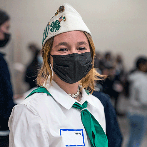 A student, dressed in her 4-H uniform, looks at the camera with a face mask on.