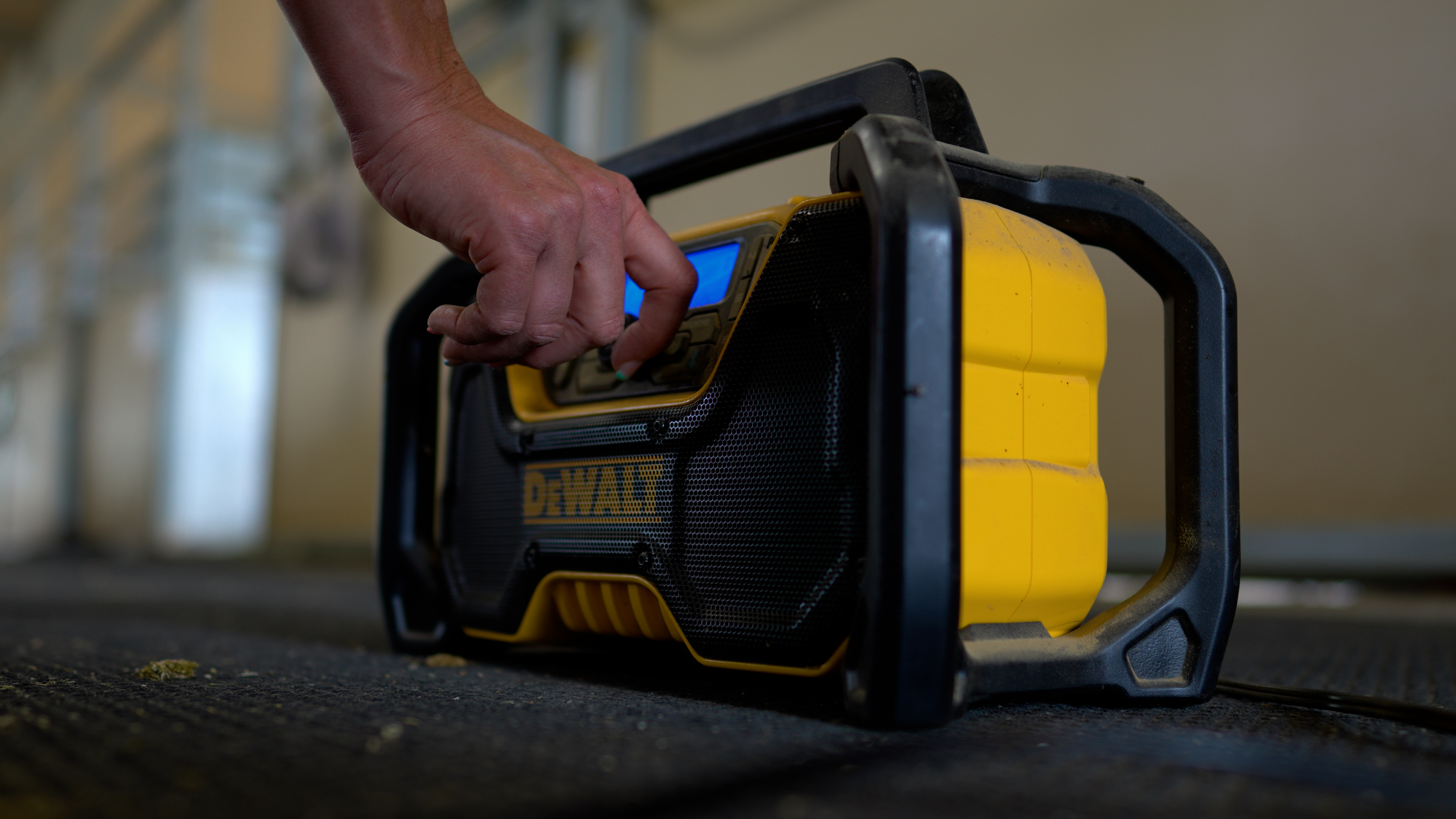 A hand adjusts the volume knob on a black and yellow DeWalt stereo.