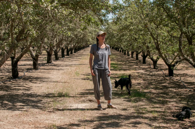 A woman with a dog standing in an orchard.