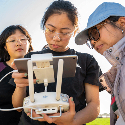 Three female students study a drone computer.