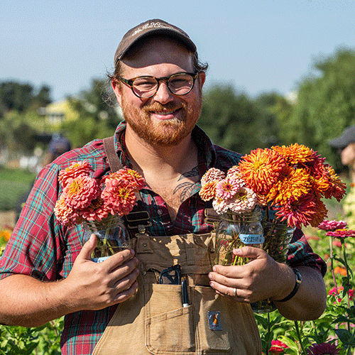Plant Sciences student and researcher Will Hazzard holds jars of zinnias.
