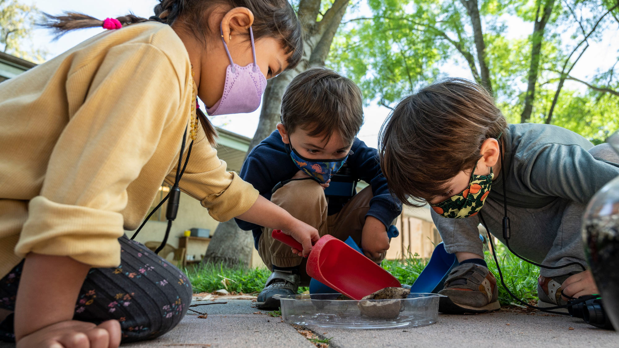 Darian, center, and Nathan, right, and a classmate examine pill bugs (affectionately known as roly-polys) that they gathered from the grounds around their outdoor classrooms.
