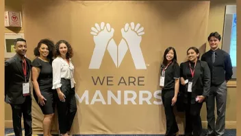 Two groups of students stand together on opposite sides of a sign that says "We are MANRRS"