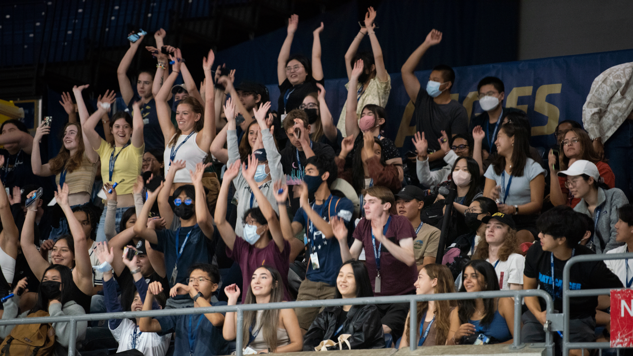 Students stand and wave their hands in the air while participating in the wave at the UC UC Center during College Welcome.
