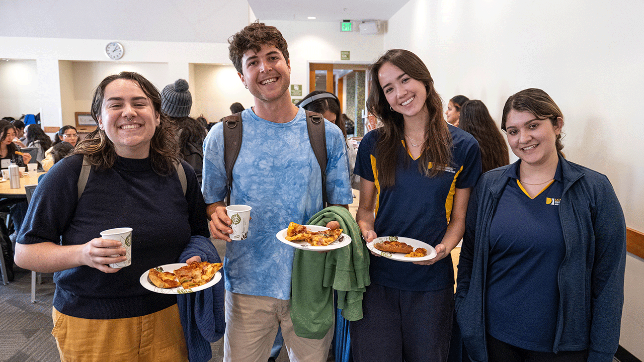 Students smile while holding plates of pizza.