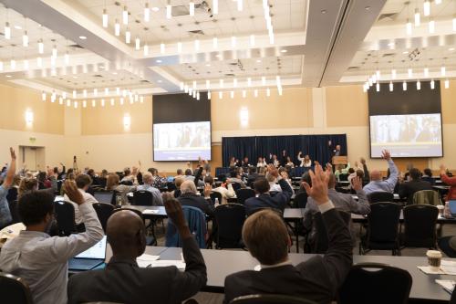 Rows of 2023 Feed Summit attendees raise their hands during a panel discussion