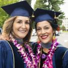 Two female graduates standing together in blue caps and gown.