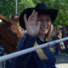 A student in a western hat waves to the parade while holding up one end of a banner.