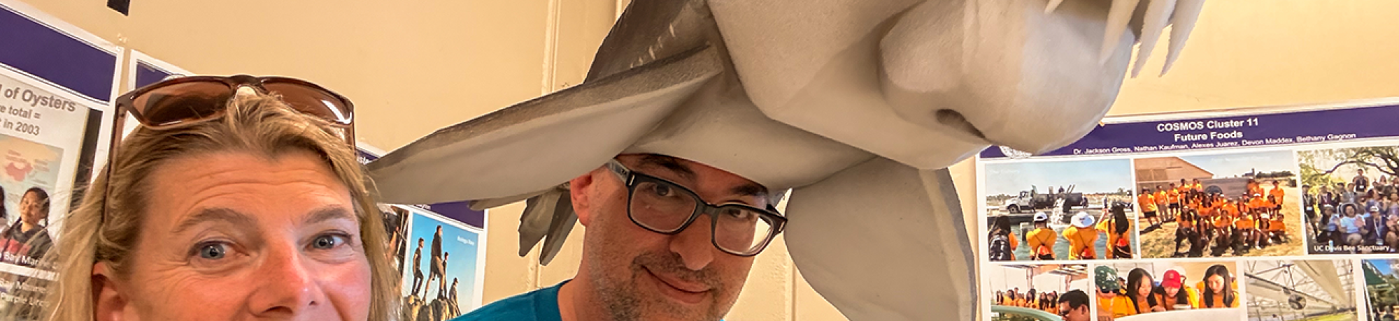 Smiling woman and man wearing oversized gray shark hat in casual indoor photo